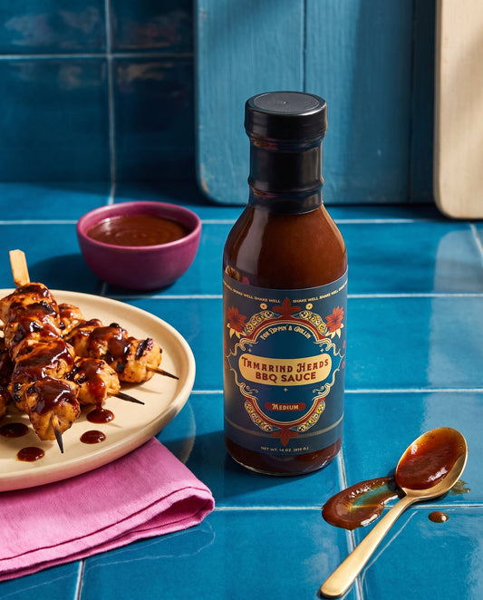 Tamarind Heads Medium BBQ sauce bottle beside grilled chicken skewers on a blue tiled kitchen counter